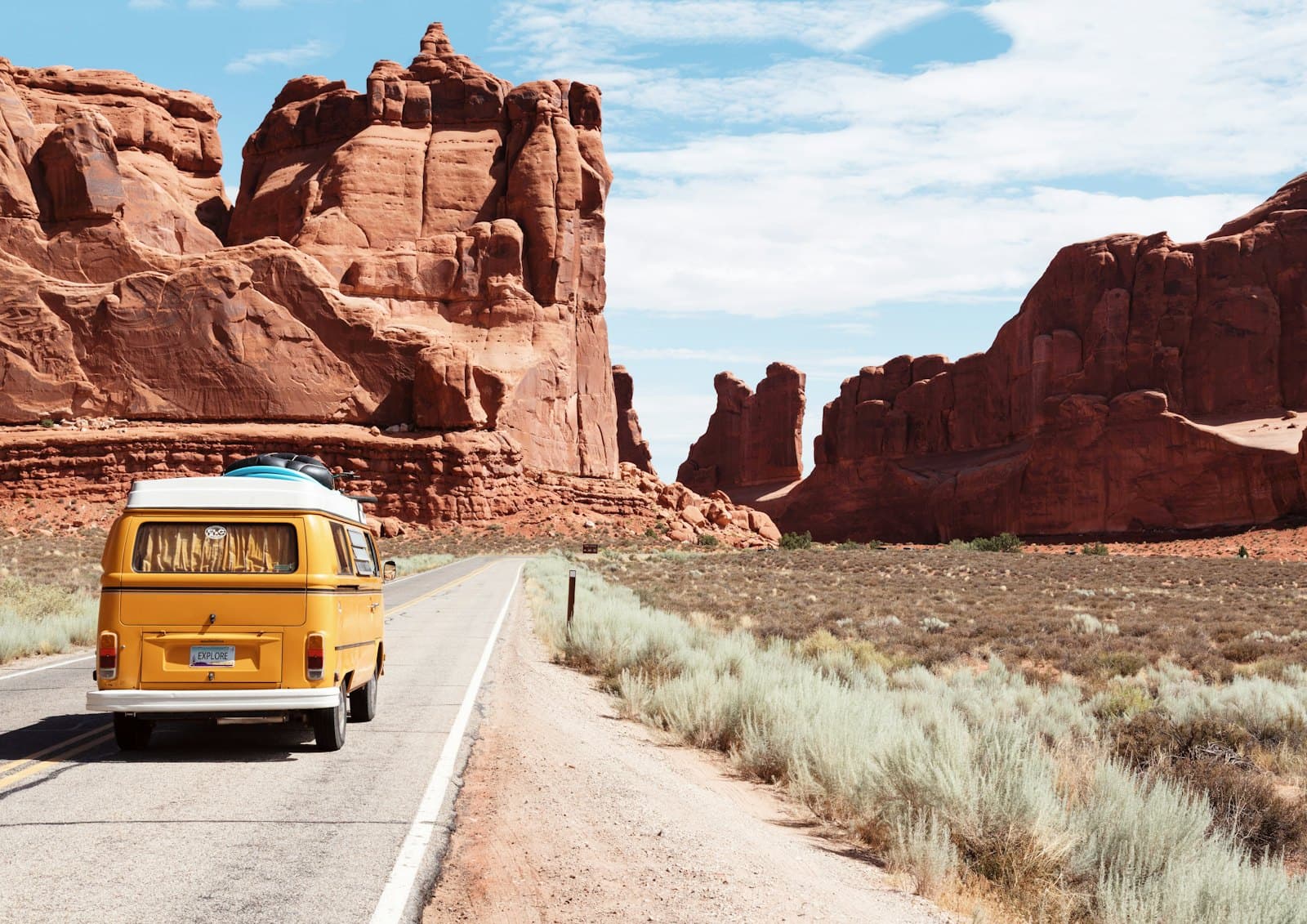 Una van amarilla avanzando por una carretera del desierto de Estados Unidos, bajo un cielo despejado